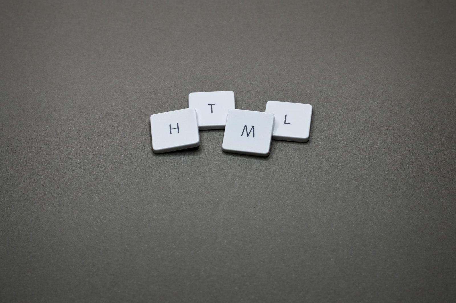 Four laptop keys with the letters h, t, m, l, on a gray background.